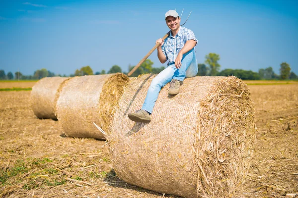 Agricultor sorridente sentado em um fardo de feno — Fotografia de Stock