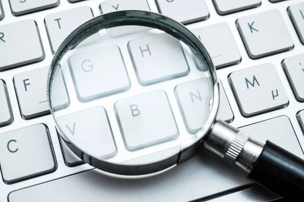 Magnifying glass on computer keyboard — Stock Photo, Image