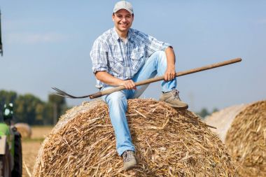 bir saman balya üzerinde oturan çiftçi gülümseyen 