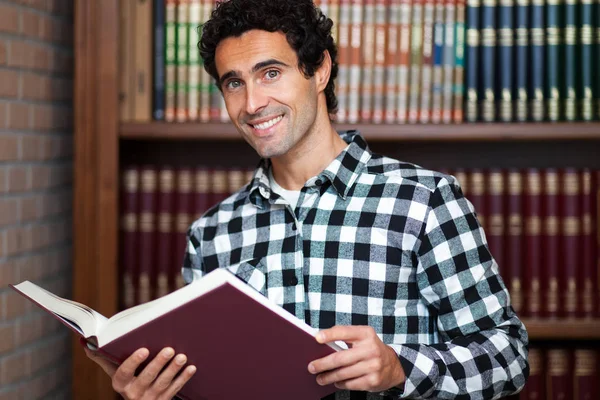 Knappe man staat bij boekenplanken — Stockfoto