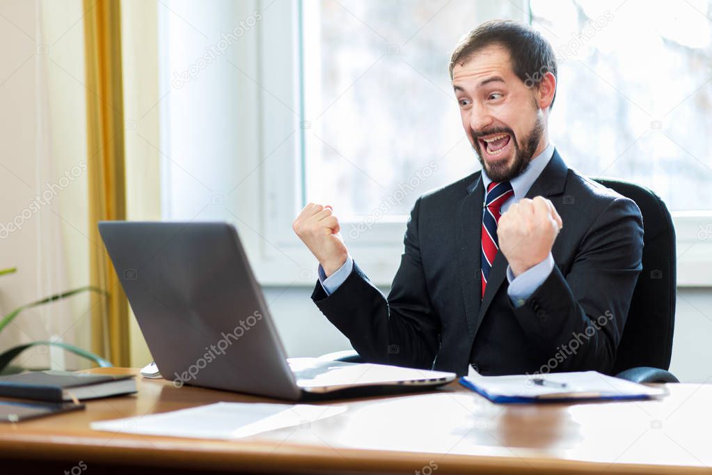 businessman cheering in front of laptop 