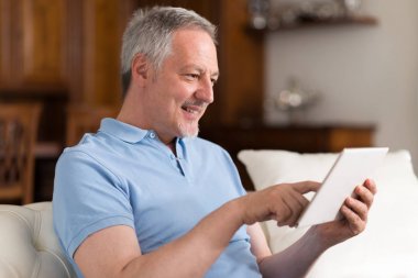 Dijital tablet dairesinde oturma odasında kullanma gülümseyen kıdemli adam portresi