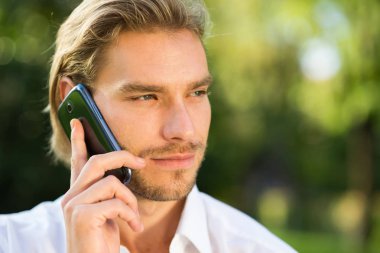 Güneşli bir günde telefonda konuşan genç yakışıklı beyaz adam portresi
