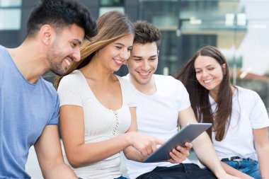 Grup genç arkadaşlar tablet birlikte modern bir şehirde bir bankta otururken kullanma