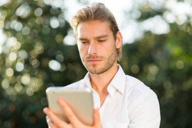 Adam parkta bankta otururken tablet bilgisayarını kullanıyor.