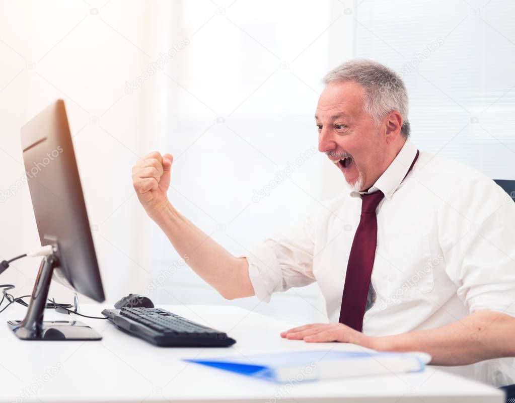 Happy businessman raising his arm in front of his computer