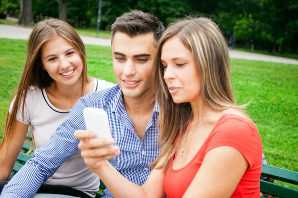 三朋友在公园里使用智能手机的肖像 — 图库照片