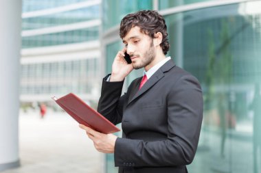 İş adamı ajandasını okurken telefonda konuşuyor.