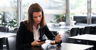 Kahve molasında olan genç iş kadını akıllı telefonunu kullanıyor.