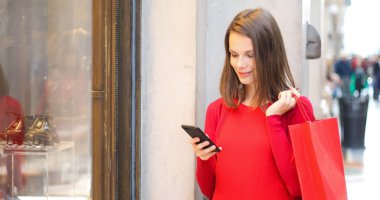 Şehirde alışveriş yaparken akıllı telefonunu kullanan genç bir kadın.