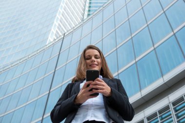 Gülümseyen genç iş kadını cep telefonunu kullanıyor.