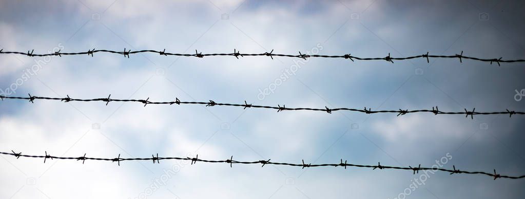 Fence with barbed wire over sky 
