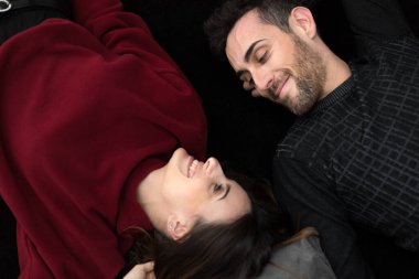 Mutlu, rahat, çekici bir adam ve kadın siyah bir halıya sırtüstü uzanmış gülümsüyor.