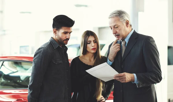 Car dealer reading a contract to a couple in an auto showroom