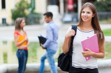 Bayan öğrenci dışarıda gülümsüyor. 