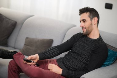 Gülümseyen bir adamın portresi, evde izlemek için bir program seçiyor.