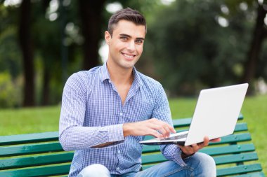 Genç adam açık havada bir dizüstü bilgisayar kullanarak