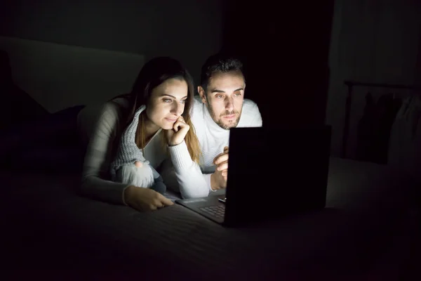 Couple watching a movie on their laptop at night while on the bed