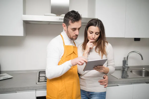 幸せなカップルを探しているレシピ上のタブレットで調理する彼らのキッチン — ストック写真