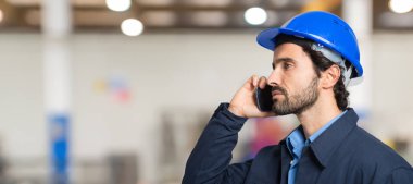 Fabrikada telefonla konuşan bir makine işçisinin portresi.