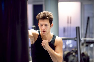 Spor salonunda çıplak elleriyle kum torbasında antrenman yapan bir adam.