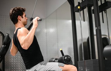 Adam spor salonunda omuzlarını ve sırtını çalıştırmak için düz makine kullanıyor. Vücut geliştirme ve doğal fitness konsepti.