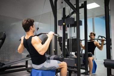 Adam spor salonunda omuzlarını ve sırtını çalıştırmak için düz makine kullanıyor. Vücut geliştirme ve doğal fitness konsepti.