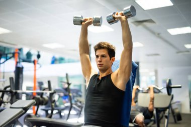 Vücut geliştirici, spor salonunda kollarını çalıştırmak için dambıl kullanıyor.