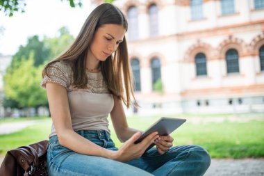 Parkta dijital tablet kullanan genç bir kadının portresi