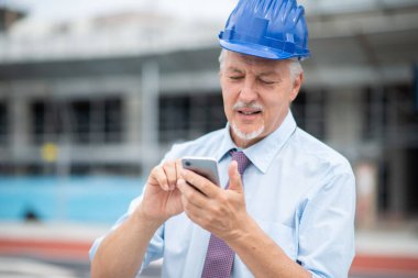 Architect using his cell in front of a construction site