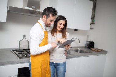 Mutfakta pişirmek için tablette yemek tarifi arayan mutlu bir çift.