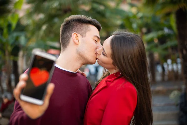 Young Couple Kissing While Showing Smartphone Heart Shape Dating Application — Stock Photo, Image