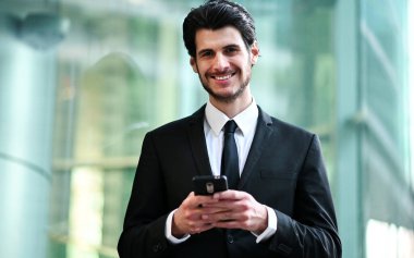 Açık havada akıllı telefon kullanan yakışıklı genç bir yönetici.