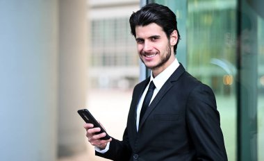 Açık havada akıllı telefon kullanan yakışıklı genç bir yönetici.
