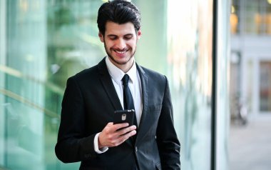 Açık havada akıllı telefon kullanan yakışıklı genç bir yönetici.