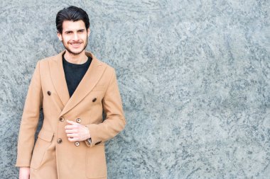 Dışarıdaki duvarın önünde gülümseyen adam.