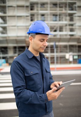 Site yöneticisi bir şantiye önünde tabletini kullanarak