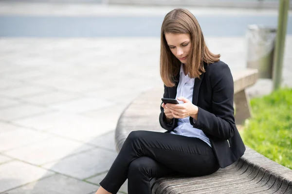 Деловая Женщина Сидя Скамейке Перед Своим Офисом Пользуется Мобильным Телефоном — стоковое фото