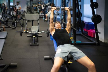 Vücut geliştirici, spor salonunda kollarını çalıştırmak için dambıl kullanıyor.