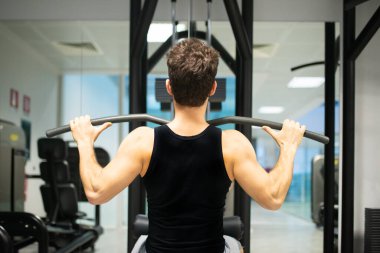 Adam spor salonunda omuzlarını ve sırtını çalıştırmak için düz makine kullanıyor. Vücut geliştirme ve doğal fitness konsepti.