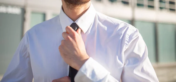 Businessman adjusting his necktie outdoor in a modern business environment, career and job interview concept