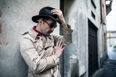 Dedektif casus adam kenar mahallede eski bir duvara yaslanıyor.