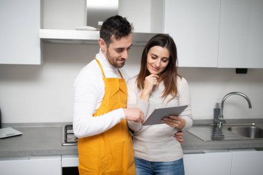 Mutfakta pişirmek için tablette yemek tarifi arayan mutlu bir çift.