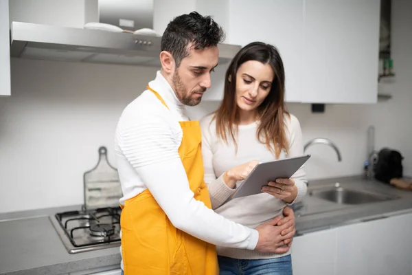 一对快乐的夫妇正在厨房里寻找平板电脑上的菜谱 — 图库照片