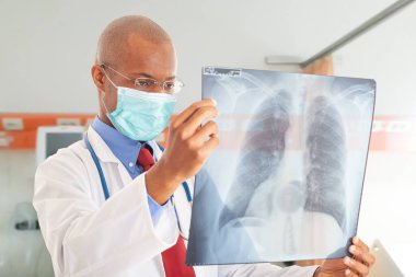Doktor akciğer radyografisi, koronavirüs ve zatürree konsepti tutarken maske takıyor.