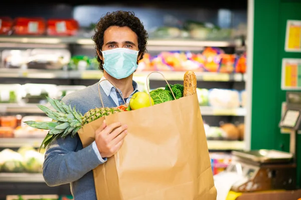 Masked man holding an healthy food bag in a supermarket during the coronavirus pandemic