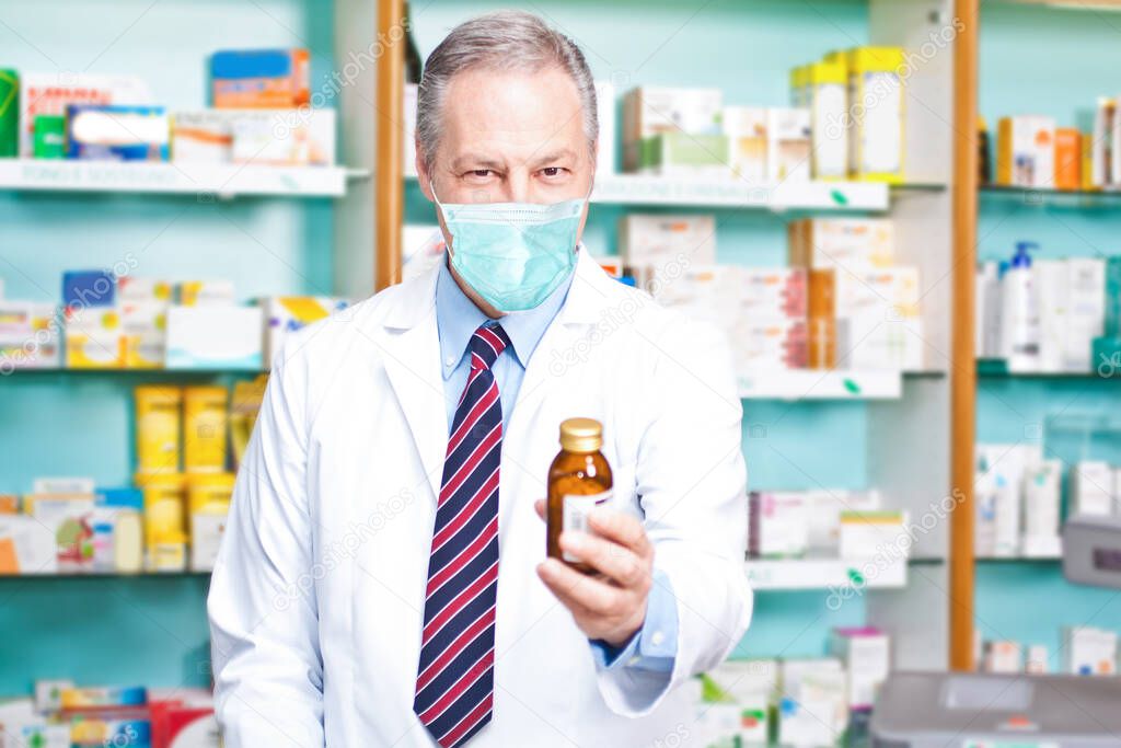 Masked pharmacist holding a bottle of medicine, coronavirus cure concept