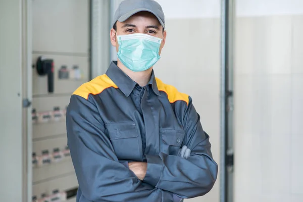 マスクを着用しながら工場内の産業用電気パネルの前にいる電気技師の肖像 コロナウイルスパンデミックの概念 — ストック写真