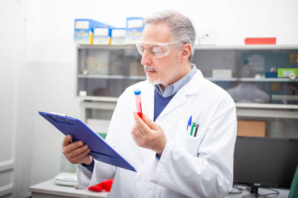 Medical scientist researcher looking at a blood tube, coronavirus blood test concept