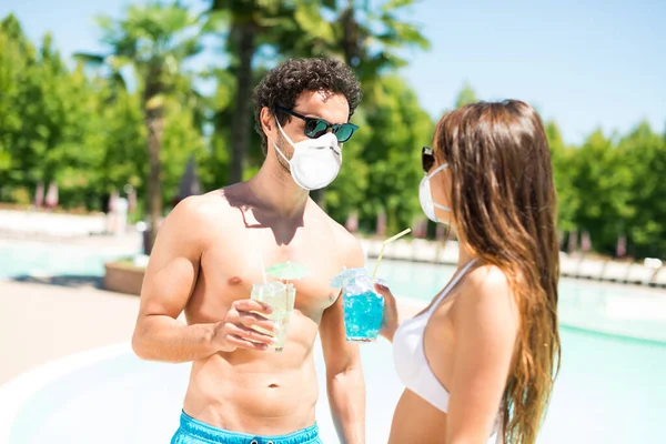 Young masked people talking in front of a pool, funny coronavirus pandemic concept during summer